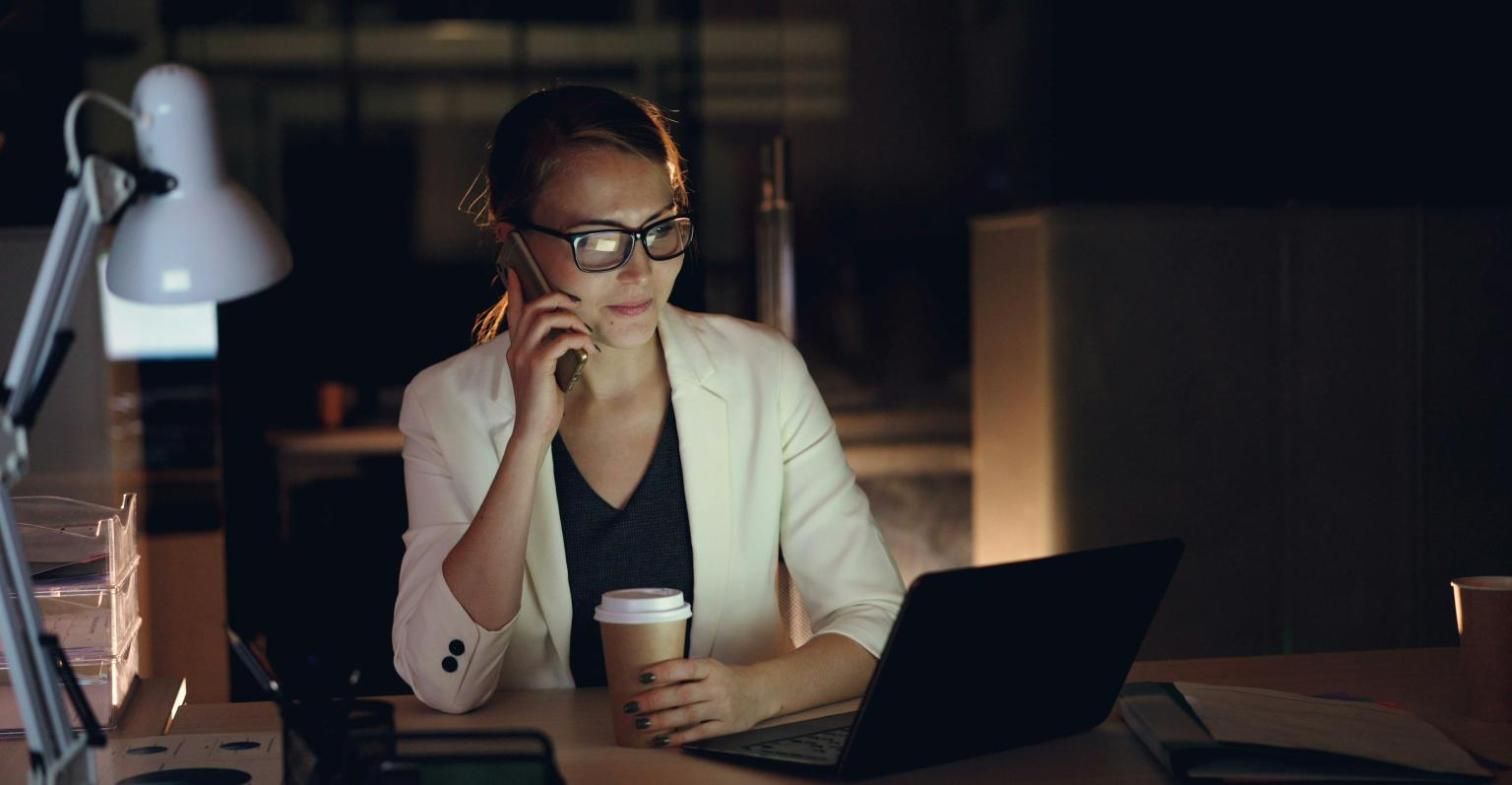 Mujer hablando por teléfono junto a su portátil y un café en la oficina
