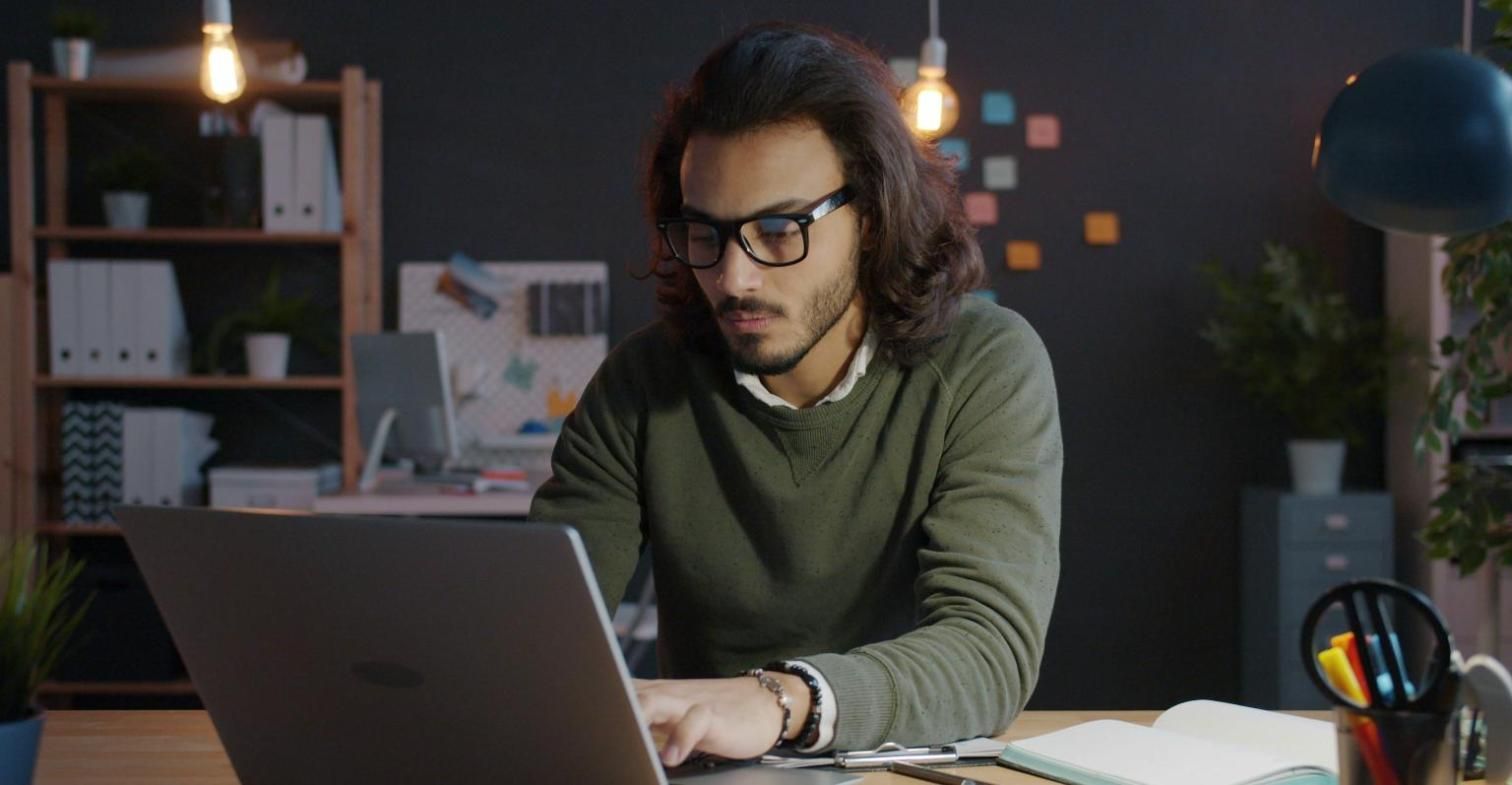 Hombre con gafas trabajando concentrado en su portátil en una oficina con luz cálida
