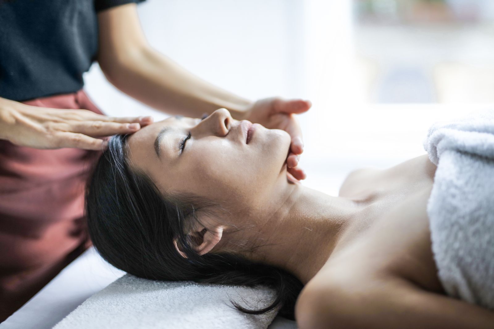 Mujer relajada con los ojos cerrados recibiendo un masaje facial en un spa