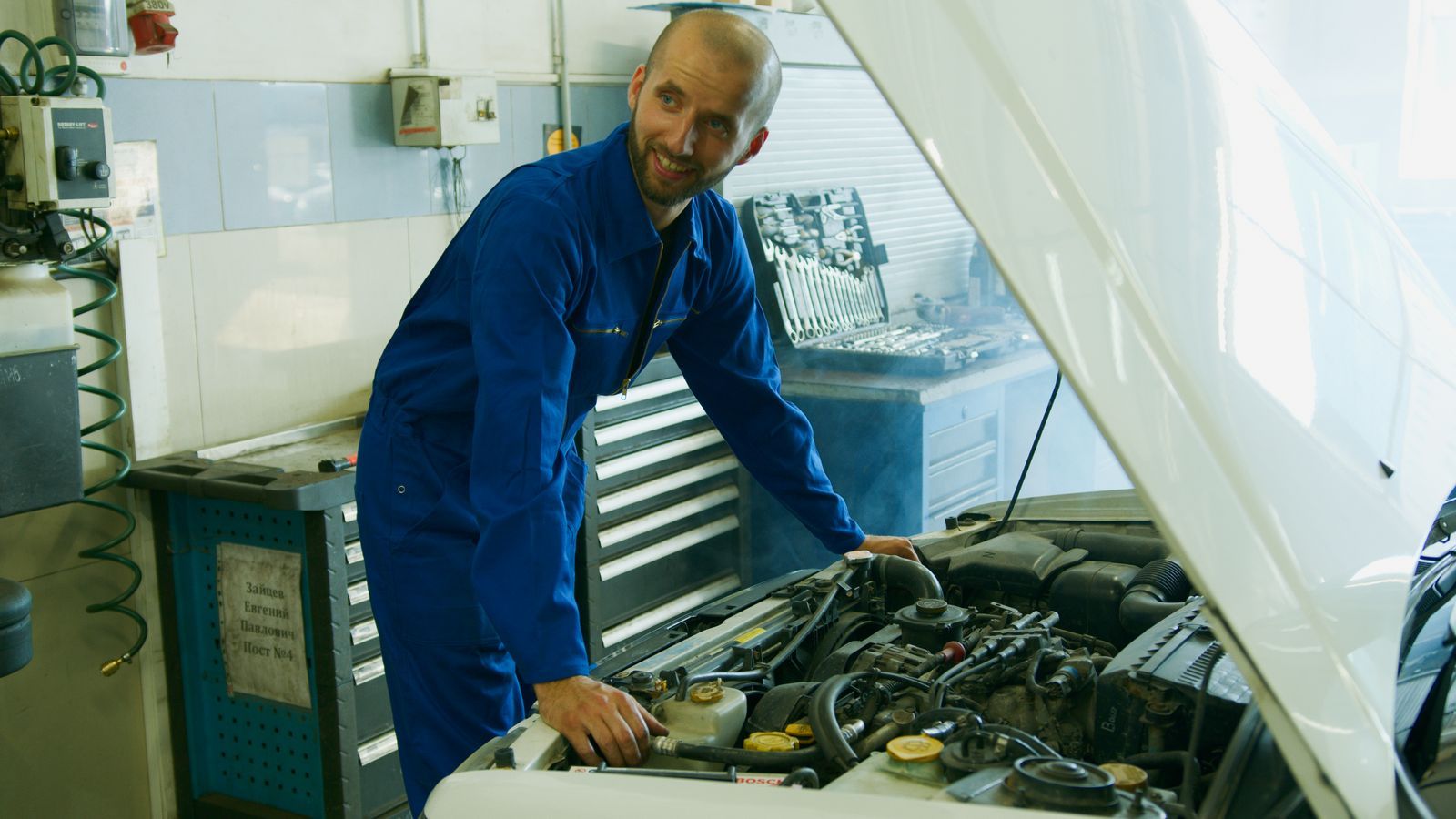 Mecánico sonriente con mono azul revisando el motor de un coche en un taller